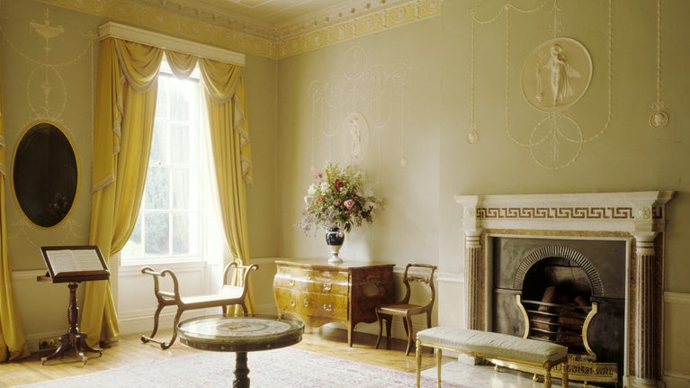 The Drawing Room, Ardress. View towards the fret pattern chimney piece, with a c18th Italian walnut commode, Regency ormolu mounted round table & Regency lyre-armed window seats.